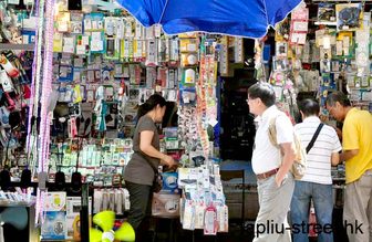 Shoppers browsing a market stall of packaged electronic accessories and cables on Apliu Street