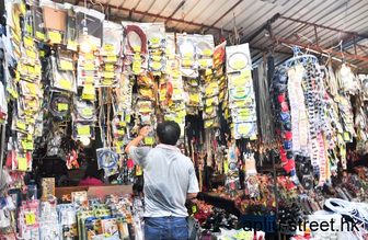 A shopper examining hanging cables and adapters at a stall on Apliu Street